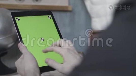 一个不知名的年轻人的手在笔记本电脑上轻敲和滚动，银球旁边的木桌上有绿色的屏幕视频