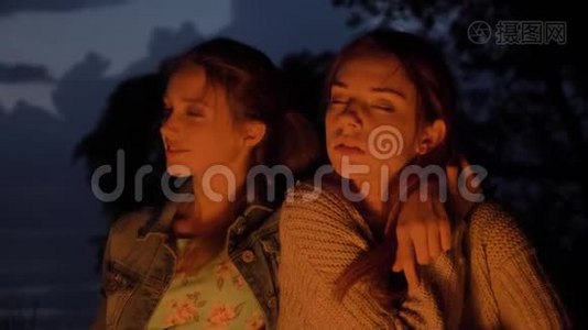 两个白种人年轻女孩晚上坐在大自然的火炉旁，看着镜头，画像视频