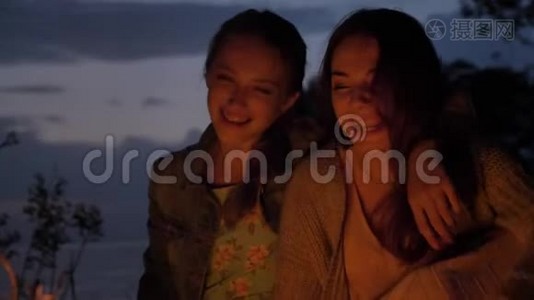 两个白种人年轻的女孩在晚上坐在大自然的炉火旁，笑着，微笑着视频
