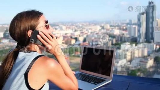 一位女性在屋顶咖啡馆的电脑上工作，一边打电话，一边观看芭堤雅的全景视频