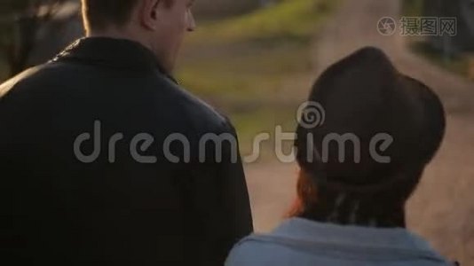 一对年轻夫妇牵着手，慈爱地微笑着走在秋天的公园里。 中弹。 后景。视频