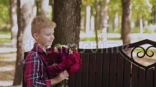 美丽的小男孩在公园里的长凳上给他心爱的母亲一束花。视频