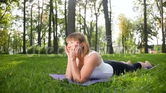 阳光明媚的夏日，中年微笑妇女在公共公园练习瑜伽的4K慢动作镜头。 身体的概念视频