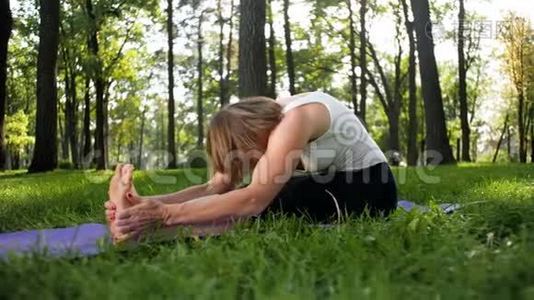 在公园的健身垫上伸展快乐微笑的女人的4K镜头。 中年妇女在森林做瑜伽练习。视频
