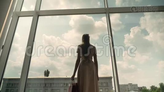年轻漂亮女孩的剪影走进商场的橱窗，手拿包包，购物理念，时尚理念，底景视频