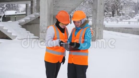 两名女检查员在冬季在施工现场检查和检查施工计划。视频