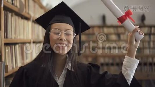 穿着学术礼服的女生微笑着站在图书馆里。视频