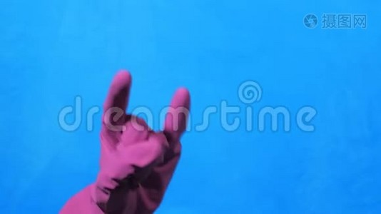 干净的手在蓝色背景上的紫色橡胶手套。 岩石和金属的手势。视频