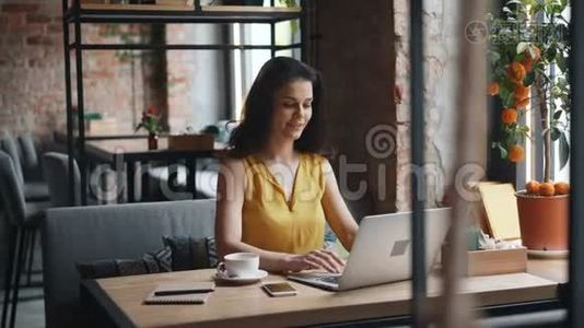 漂亮的女孩用笔记本电脑打字，微笑着独自在咖啡馆工作视频