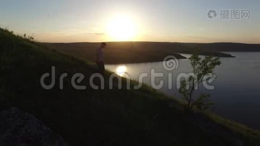 空中史诗拍摄一个人在河岸边散步，作为一个轮廓在美丽的日落。视频