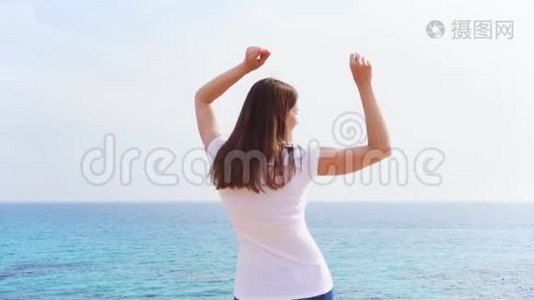 阳光明媚的一天，女人在悬崖上与蔚蓝的大海欢快地跳跃。 无护理女性慢动作舞蹈视频
