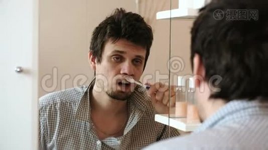 刚醒过来的一个宿醉的困人正在刷牙，看着镜子里的倒影。视频