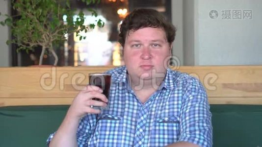 胖子拿着一杯碳酸软饮料可乐，坐在咖啡馆里。 饮料和健康。视频