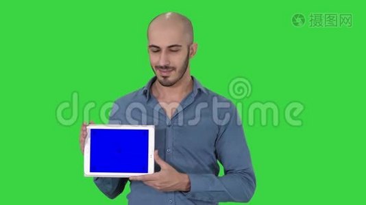 微笑休闲男子呈现一个平板电脑与空白屏幕上的绿色屏幕，铬键。视频