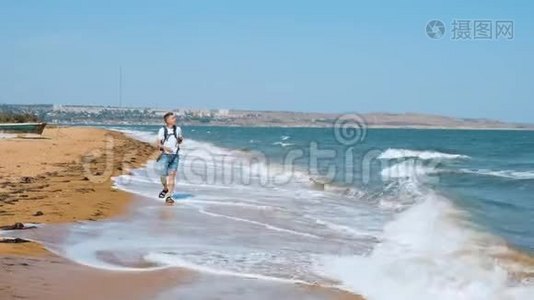 一个年轻人走在沙滩上，用手机拍了一只海鸥。视频