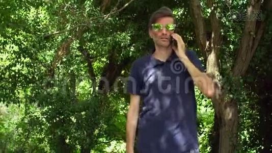 在森林或公园里的智能手机上戴着太阳镜的有魅力的、情感成熟的男人交谈视频