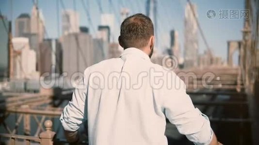 从后视图的成年白种人男子站在布鲁克林大桥栏杆，享受惊人的城市景观和步行4K。视频