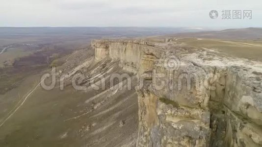 年轻女子坐在高高的岩石墙边。 空中观景台。 无人机快速向后飞行视频