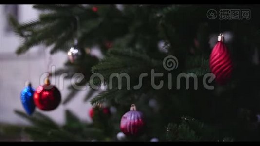 把圣诞装饰品挂在有圣诞灯的树上。 小女孩的手装饰圣诞树，特写视频