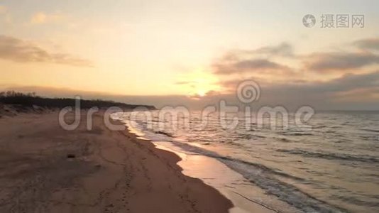 空中观看无人机镜头低飞行在一个废弃的海滩上日落。 带着滚滚海浪和夕阳的沙岸视频