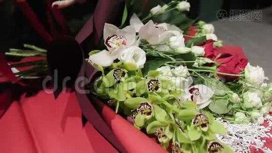 花商把一条丝带系在兰花兰花、红白玫瑰和香果的一束美丽的花束上视频