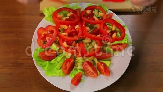 女用手把红椒圈放在盘子里，里面放着生菜和西红柿。视频