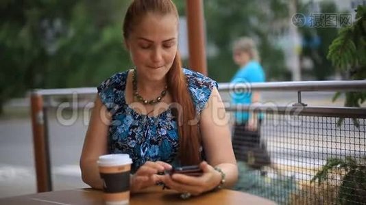 一个红头发的漂亮女人坐在街头咖啡馆的桌子旁喝咖啡。视频