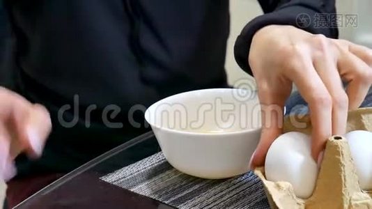 女人的手在厨房把一个鸡蛋打碎成一个白色的陶瓷碗视频