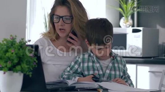 女人把教养孩子和工作结合起来，母亲用手机用电脑说话，而儿子在她身边玩耍视频