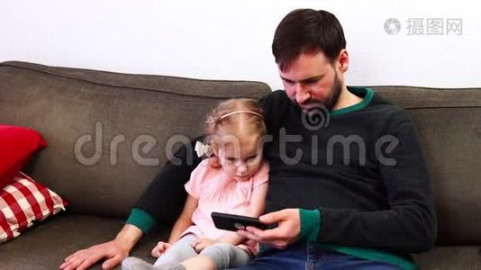 父亲和女儿看着坐在沙发上的智能手机视频