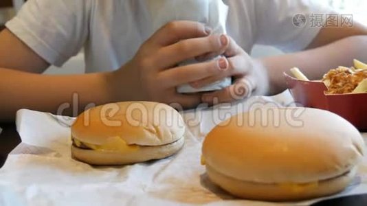 青少年在快餐店里吃一个大鸡卷。 桌子上有大的芝士汉堡和薯条。视频