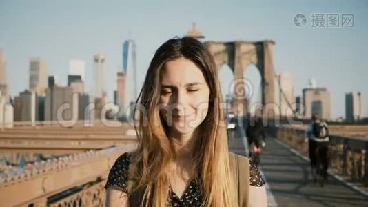 年轻的欧洲旅游女孩，背包在相机摆姿势，触摸头发和微笑布鲁克林大桥，纽约4K。视频