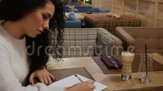 一个头发卷曲、深褐色的可爱女孩正在餐馆里写一首诗视频