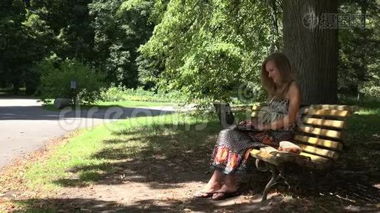 学生女孩工作与笔记本电脑坐在绿色公园的长凳上。 4K视频