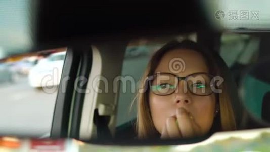 戴眼镜的漂亮女孩在车里画嘴唇，在镜子里检查她的外表视频