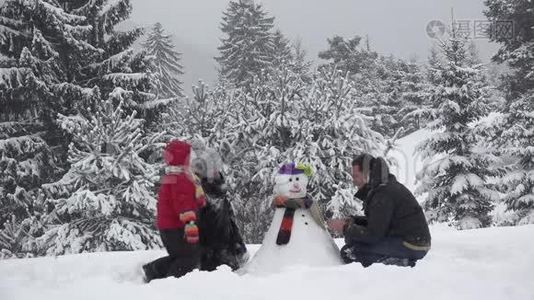 一家人在公园里堆雪人，可爱的孩子固定纽扣，下雪的树，美丽的冬天的家庭肖像，真正的团队合作视频