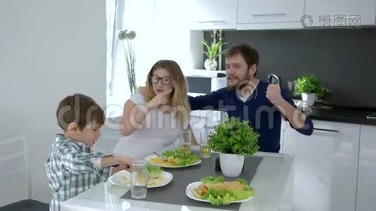 健康的食物，快乐的爸爸妈妈和儿子一起吃厨房里刚准备好的饭菜视频