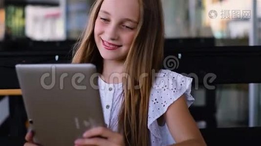 小女孩在咖啡馆里用平板电脑，微笑着视频