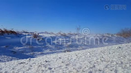 雪从路边的田野飘来，刮着雪风。 轻风吹雪朝相机..视频