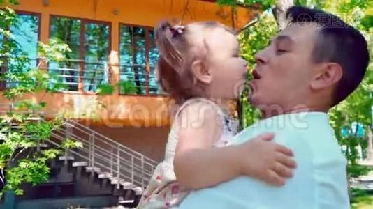 一位年轻的父亲抱着一个小女儿，在房子的背景下亲吻她视频