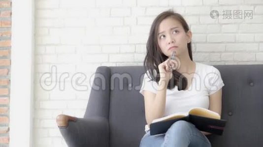 漂亮的亚洲女人坐在沙发上学习，在家里写笔记本，做家庭作业视频