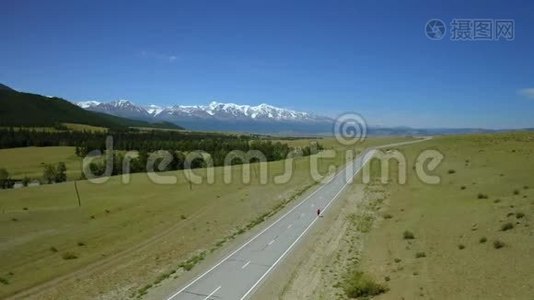 在阳光明媚的一天，在山上的柏油路上背着背包的旅行女孩的空中摄影。 全景观视频