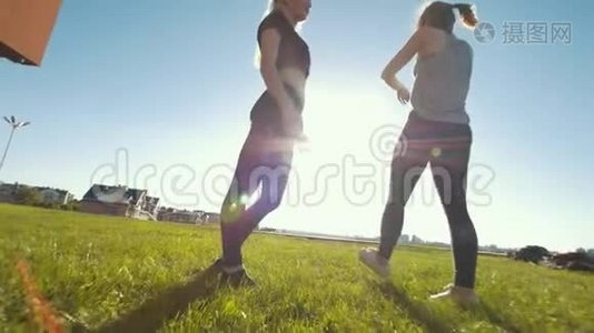 两个女杂技演员在阳光下锻炼时在草地上玩视频