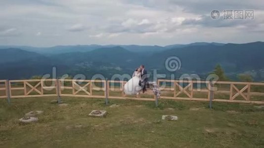 新郎和新娘坐在山岗附近的篱笆上。 空中无人机射击视频