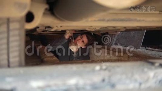 年轻的男性机械师在汽车下面，从托盘下拧开部件视频