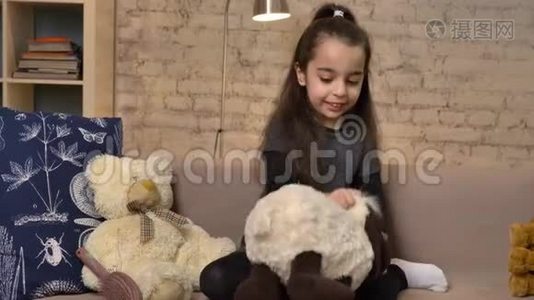 一个小女孩坐在沙发上，玩着一只泰迪羊，软玩具，背景是50fps的家庭舒适。视频