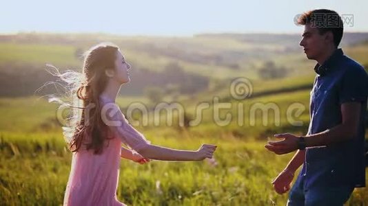 一对年轻漂亮的夫妇拥抱和亲吻，自然，日落时的田野。视频