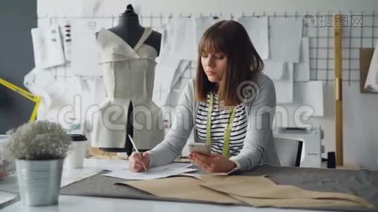 创意服装设计师在现代裁缝店缝纫时，会看智能手机和素描视频