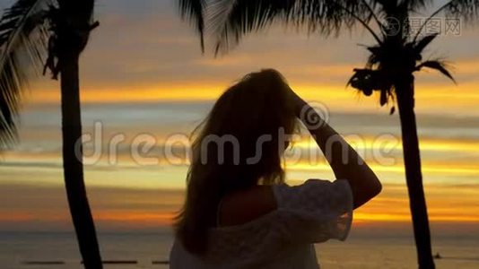 日落时分，金发女孩站在海滩上的棕榈树旁视频