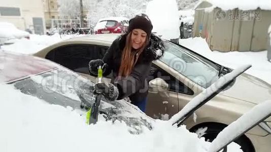 4k视频美丽微笑的年轻女子用伸缩刷子从雪中清洁汽车视频